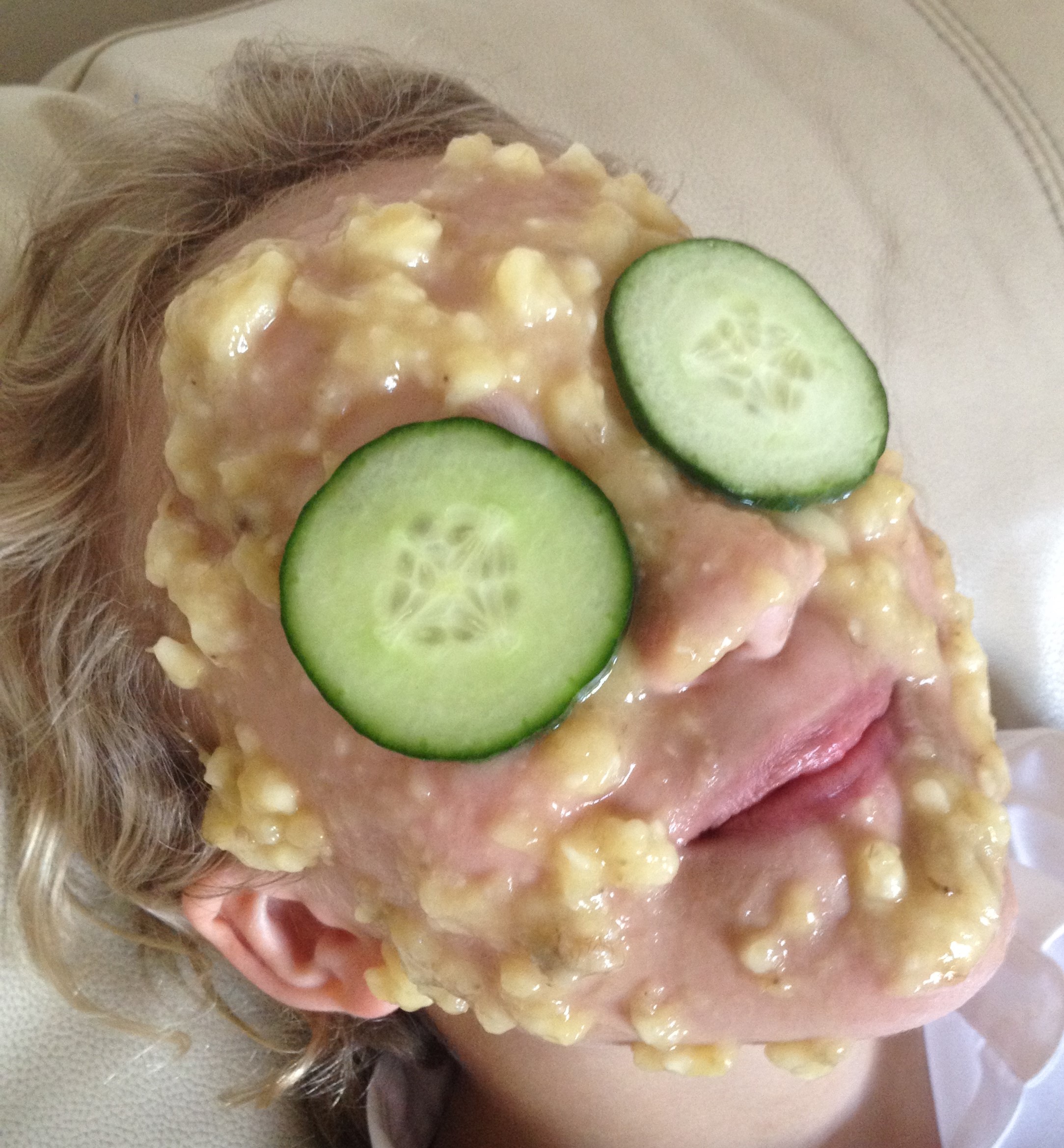 face covered in banana face mask and cucumber slices