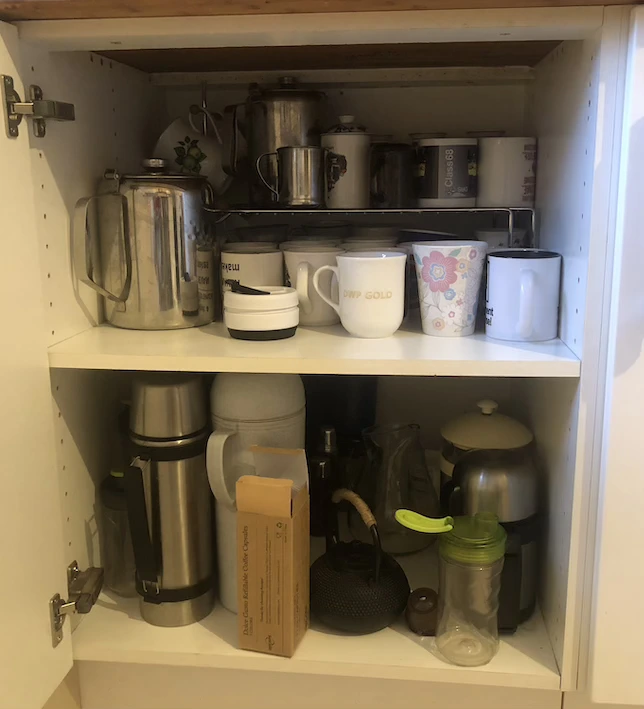 White kitchen cupboard with two shelves full of mugs, flasks and teapots