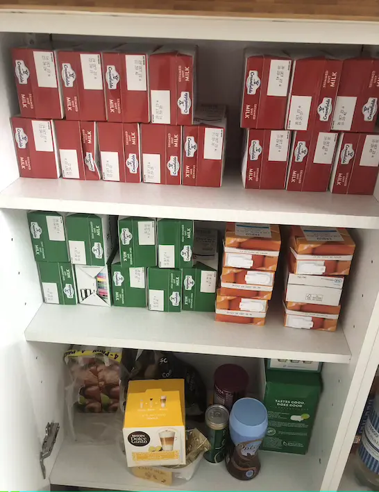 White kitchen cupboard with two shelves of baking tins, plastic storage boxs and a grater