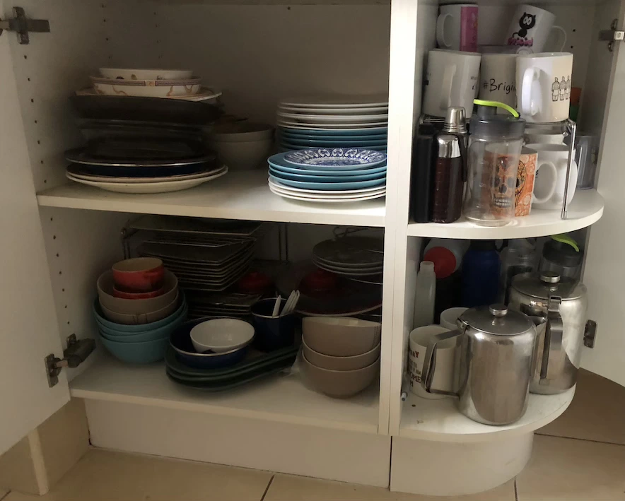 White kitchen cupboard with multiple shelves full of stacked plates, bowls, mugs and teapots