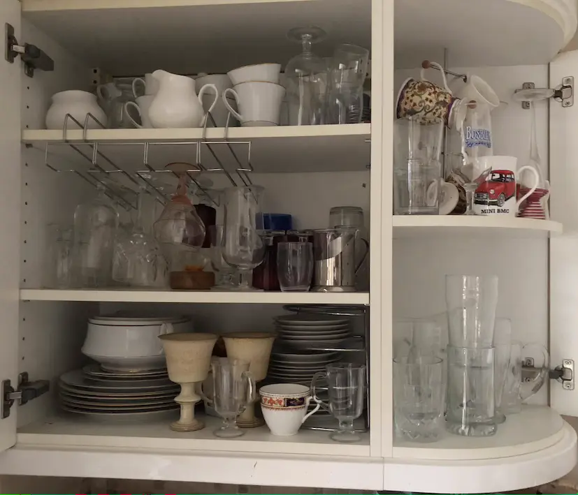 White kitchen cupboard with multiple shelves full of stacked glassware and china