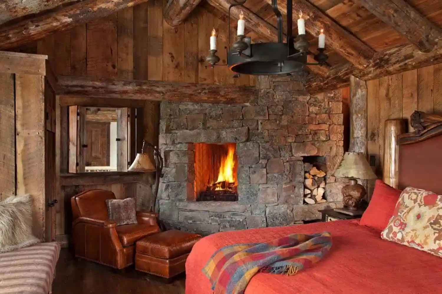 Roaring fire in the stone fireplace of a log cabin, with upholstered furniture, cushions and throws in the foreground.