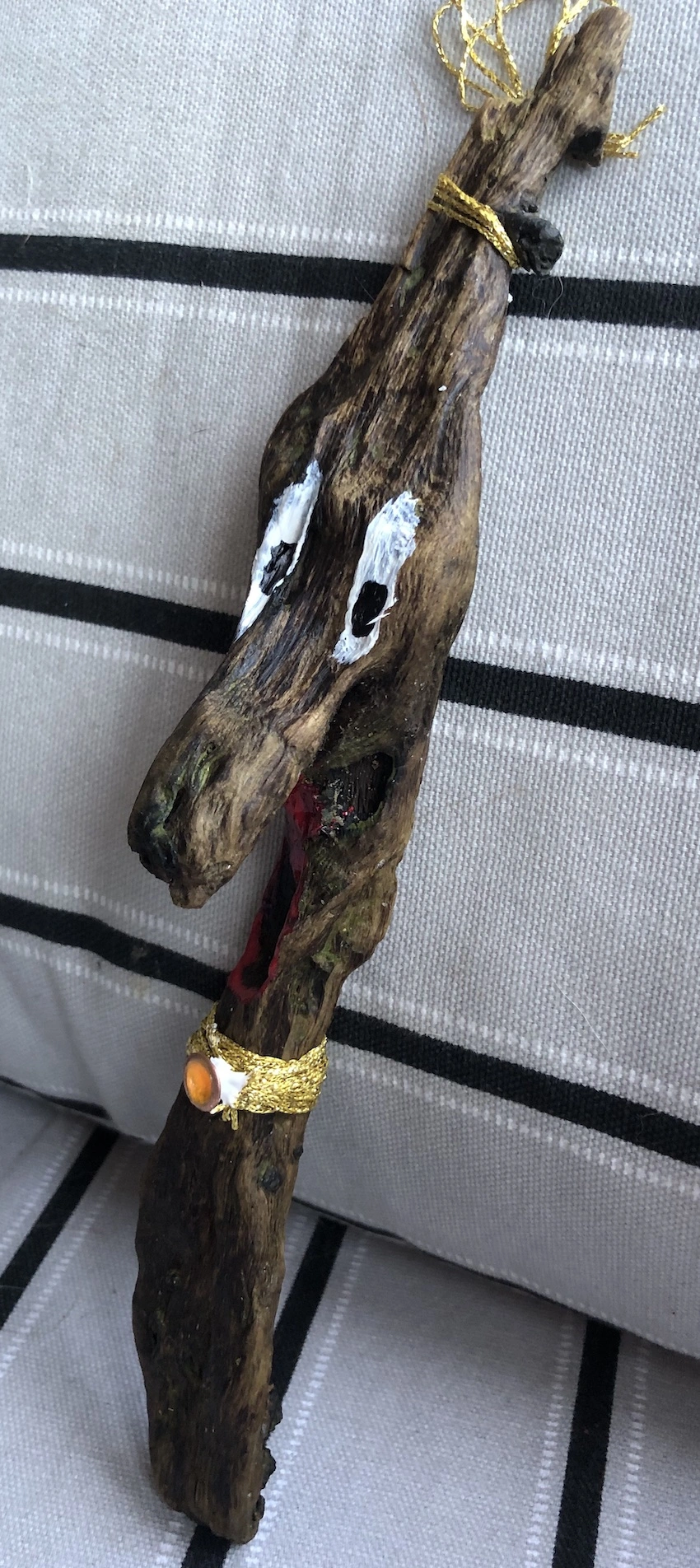 Piece of driftwood, with painted eyes and a gold collar, made to resemble an animal