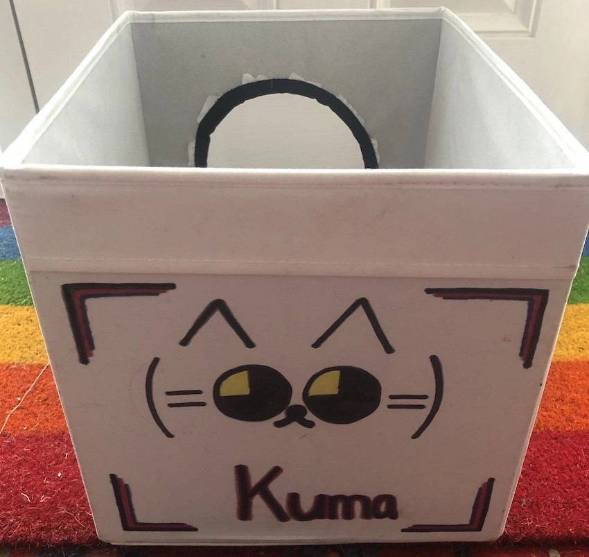 Japanese emoticon of a cat drawn in black on a white Ikea Drona cube