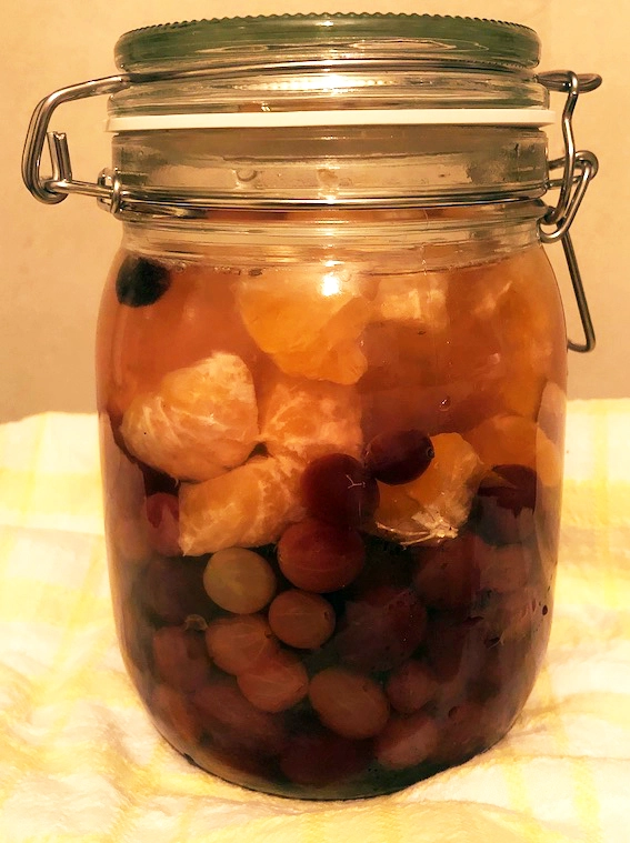 Glass preserving jar filled with red gooseberries and orange segments in liquid