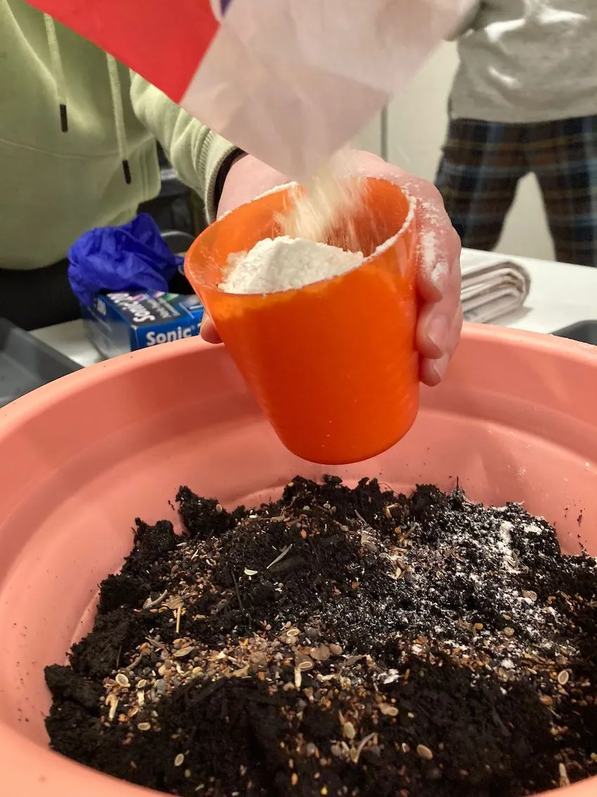 flour being poured into an orange cup held over a bowl full of compost