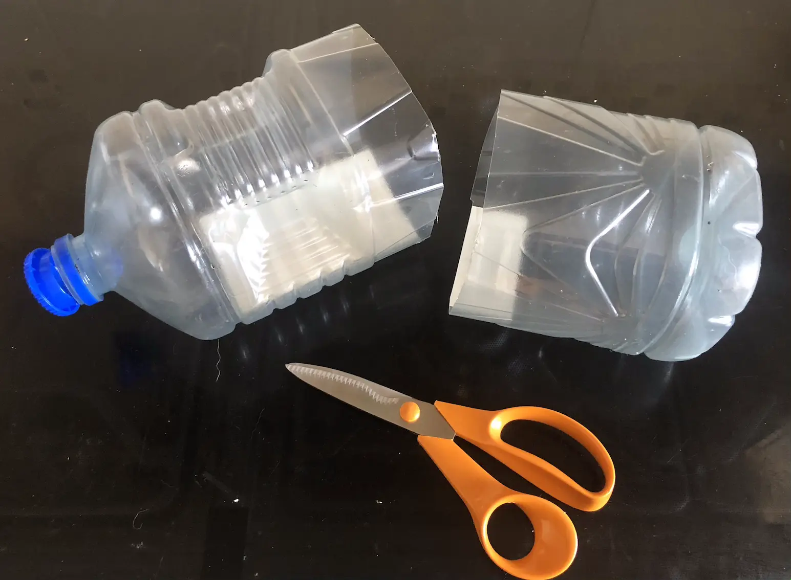 three litre plastic oil bottle, cut in half, alongside a pair of scissors with orange handles