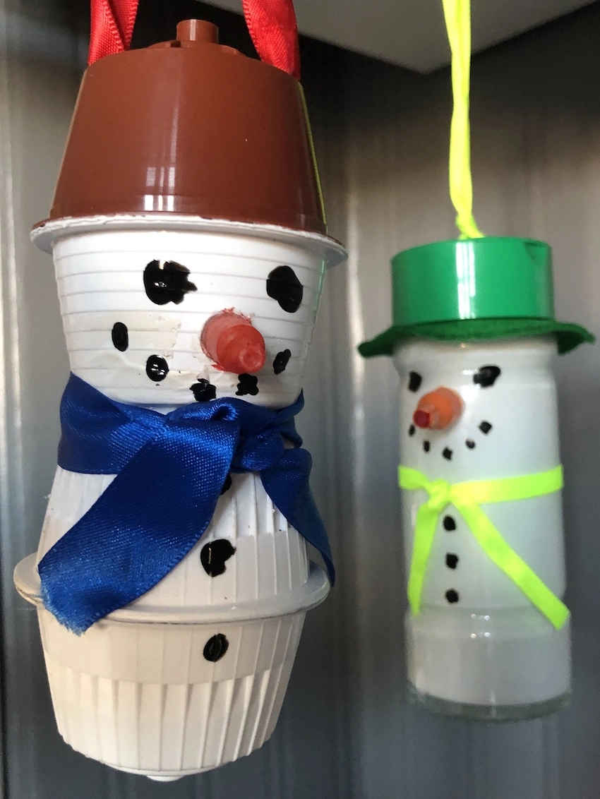 Two snowmen decorations, one made from an old spice jar and one made from multiple coffee pods