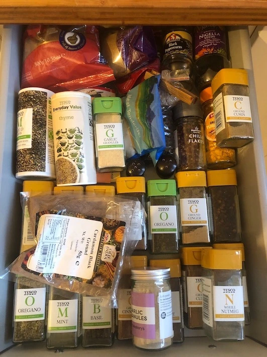 View from above of a white kitchen drawer full of spice jars and packets