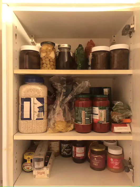 White kitchen cupboard with three shelves full of food jars and packets