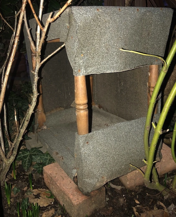 small wooden table wrapped in grey roofing felt, placed on bricks in a garden