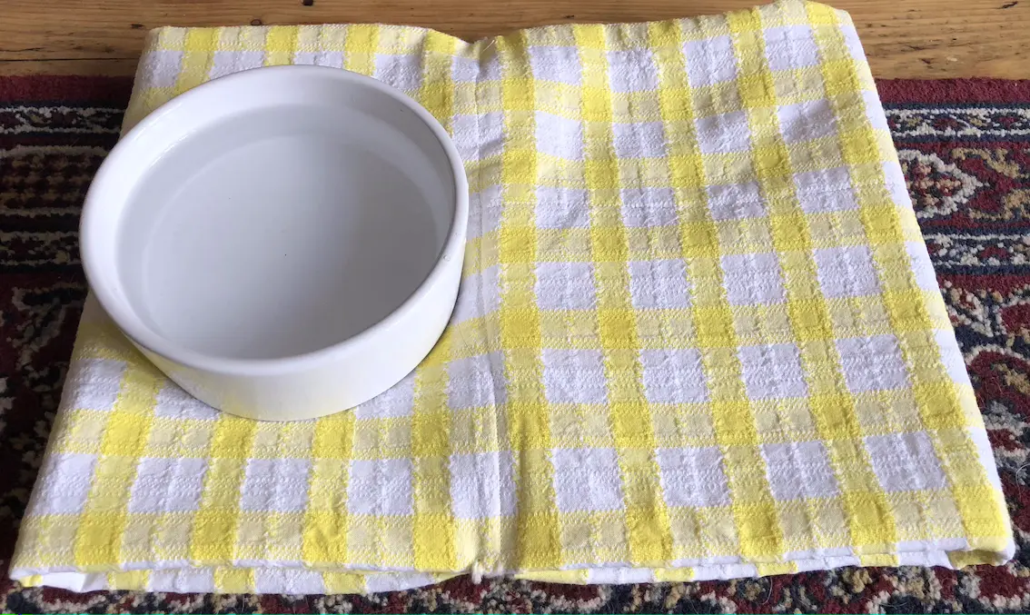 padded mat made from a yellow and white checked tablecloth with a dog's water bowl place on top