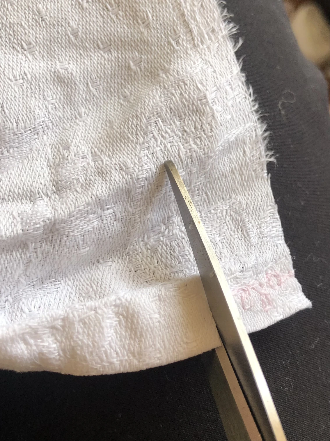 scissors cutting a narrow strip off a piece of white cloth