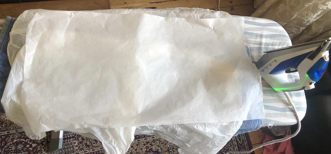 plastic bags under a sheet of greasproof paper waiting to be ironed onto a woven fabric base of a laundry bag