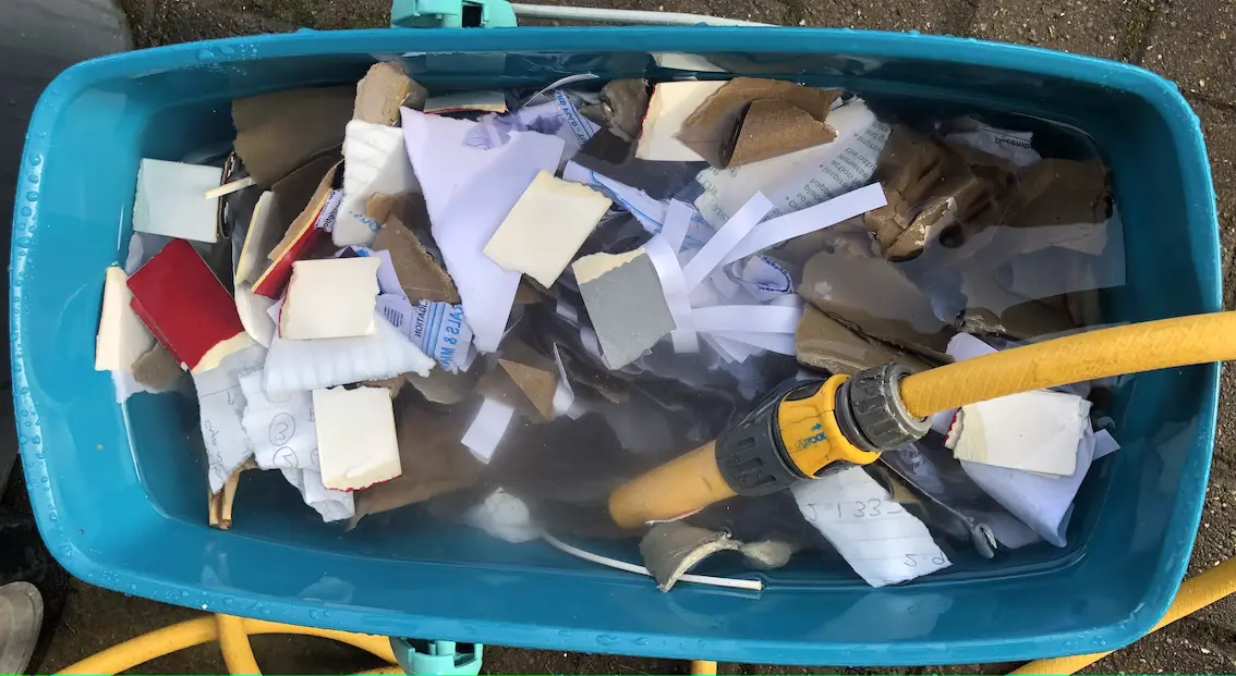 turquoise mop bucket, filled with paper, cardboard and water, with a hosepipe in one corner