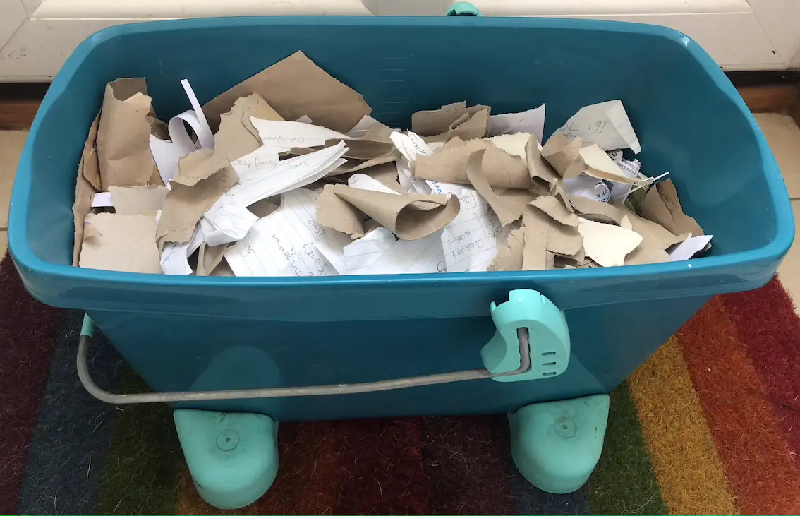 turquoise mop bucket filled with torn pieces of cardboard and paper