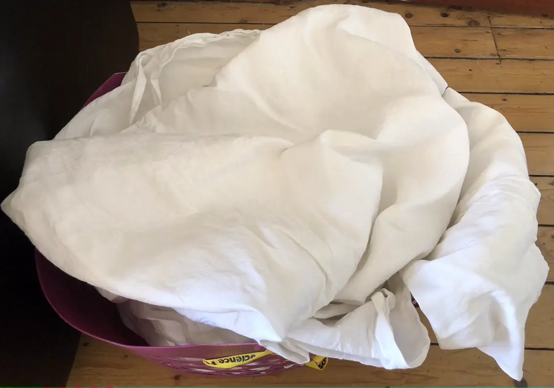 pile of white linen tablecloths in a purple laundrty basket