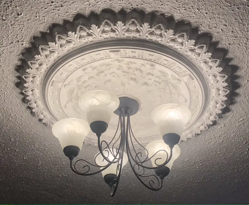 Illuminated 5 armed black metal chandelier with upturned glass globes, lit with an bright white light, below a patterned plaster ceiling rose.