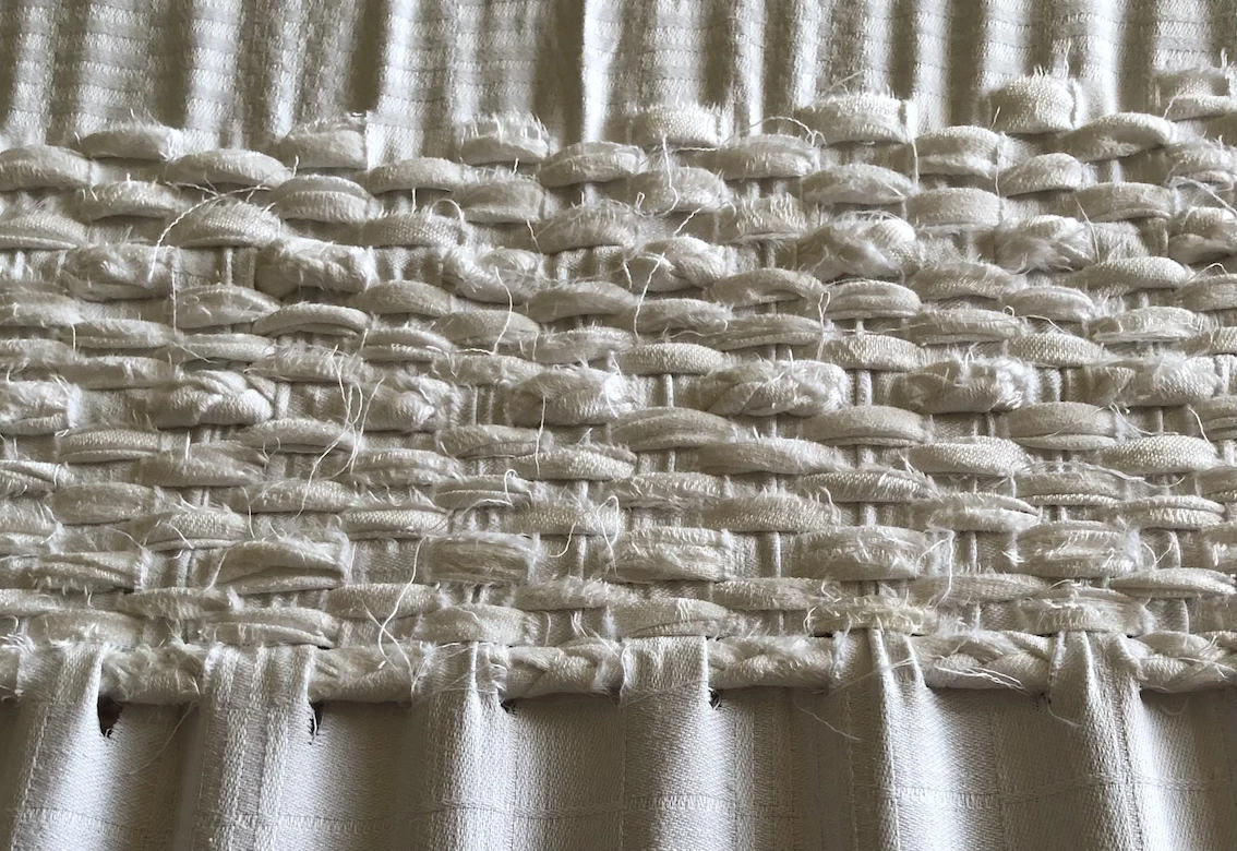 section of cloth strips woven through slits in a piece of white fabric