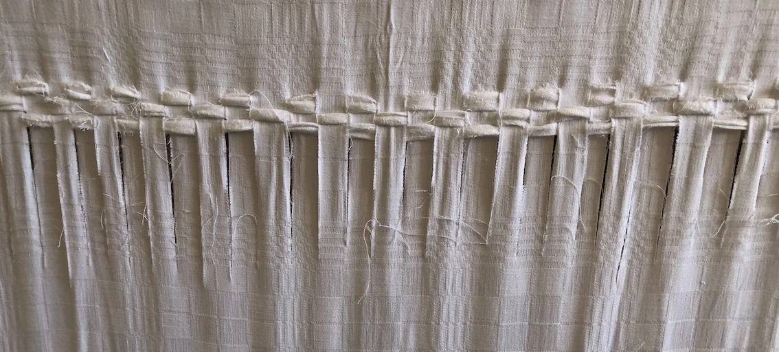 white cloth with slits cut vertically at intervals and rows of cloth woven through