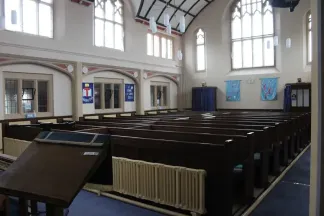 Interior of a Methodist church with dark wooden pews, cream coloured walls and large arched windows