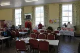 Church hall with tables and chairs in the centre and stalls around the edge in front of large windows