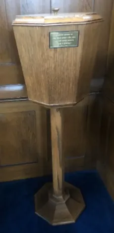 Wooden octagonal baptismal font on a stand, bearing an inscribed brass plate