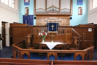 Organ pipes against a light blue wall, wooden altar rail in the foreground and wooden panelled pulpit and choir stalls behind