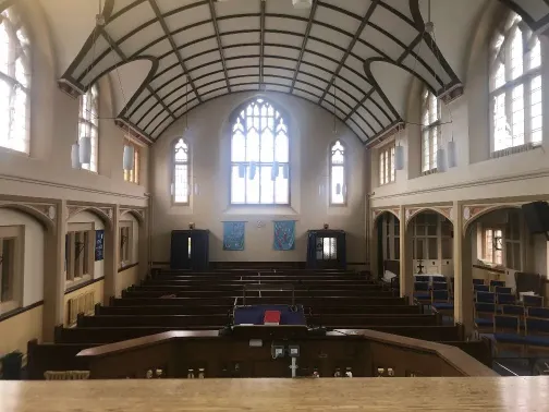 Interior of a Methodist church with dark wooden pews, cream coloured walls, a curved ceiling and high arched windows