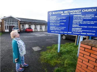 Woman in jeans, a blue cardigan and silk scarf standing in a church car park looking at the notice board