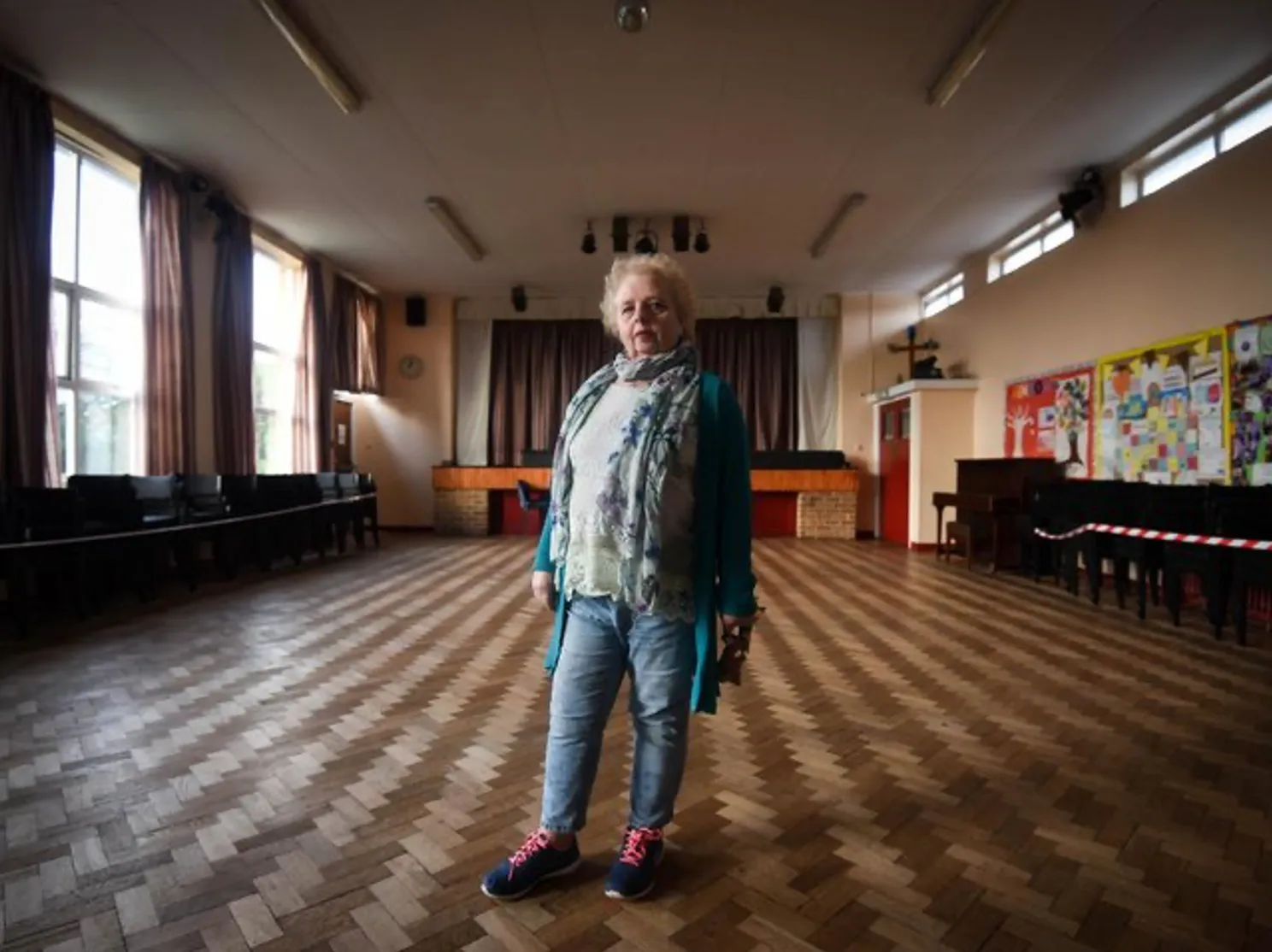Woman in jeans, a blue cardigan and silk scarf standing in an empty church hall