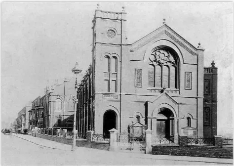 Black and white image of a church with a square tower on the corner of a road