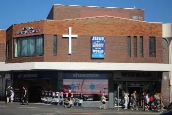 Modern red brick church building comprising the floor above a shoe shop