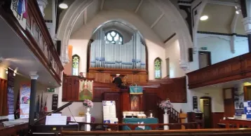 Interior of a large church with a balcony, painted white with wooden panelling and organ pipes in the centre