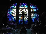 Geometric design, stained glass window behind a darkened table on with a cross is placed