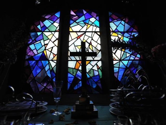 Geometric design, stained glass window behind a darkened table on with a cross is placed
