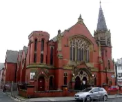 Red brick church with a spire, cars parked outside