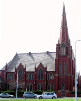 Side view of a traditional red brick church with a spire on the left hand end