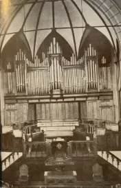 Monochrome image of organ pipes and a wooden pulpit in a church